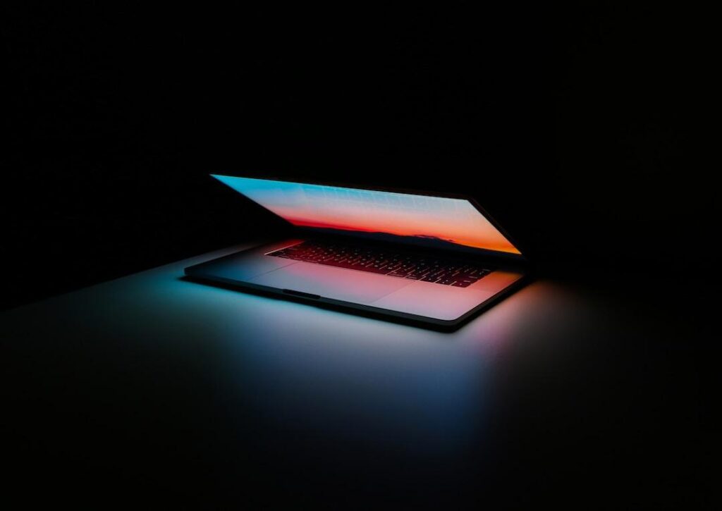 A laptop halfway open radiating light on a black background.